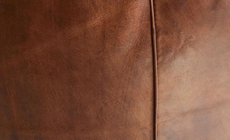 May include: Close-up of brown leather with visible grain and texture. A vertical seam runs down the center, dividing the image into two sections. The leather has a distressed appearance.