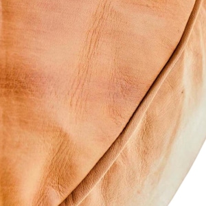 May include: Close-up of a section of tan leather, showing the natural grain and texture. The leather has a warm, golden-brown hue with subtle variations in color and a visible seam.