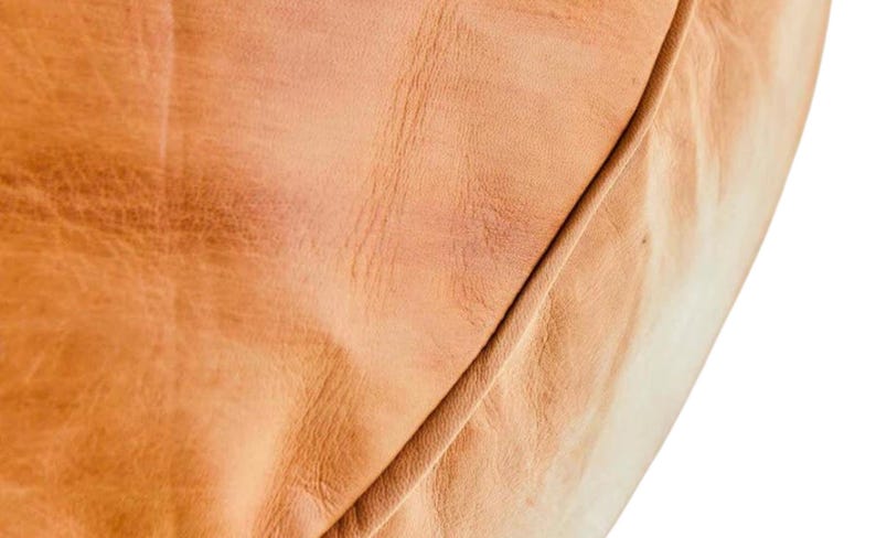 May include: Close-up of a section of tan leather, showing the natural grain and texture. The leather has a warm, golden-brown hue with subtle variations in color and a visible seam.