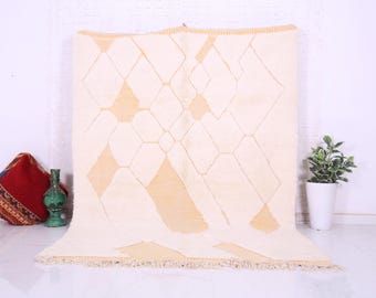 May include: A white and beige Moroccan rug with a geometric pattern. The rug has a fringe border.