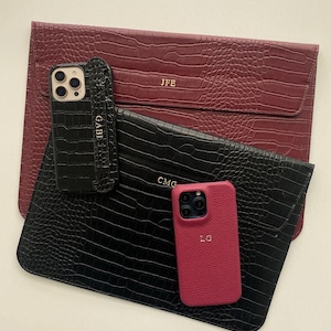 May include: A selection of personalised phone cases and a laptop sleeve, all with a faux crocodile skin texture. The colours are burgundy, black, and pink. The initials "JFE", "CMG", "GABI", and "LG" are embossed on the items.