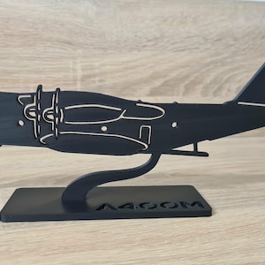 Peut inclure: Maquette en bois noire d'un avion de transport militaire A400M. Le modèle présente des découpes détaillées des hélices et des fenêtres, et est monté sur un socle noir. Le texte "A400M" est visible sur la base.