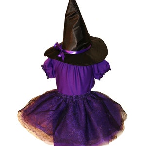 Könnte beinhalten: Ein Hexenkostüm für Kinder. Es besteht aus einem schwarzen Spitzhut mit lila Band, einem lila Oberteil mit kurzen Ärmeln und einem mehrlagigen lila-schwarzen Tüllrock. Ideal für Halloween oder zum Verkleiden.