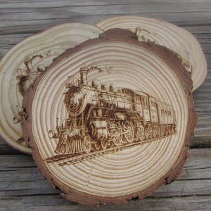 May include: Three wooden coasters with a brown wood grain pattern. The center coaster features a detailed laser-engraved image of a vintage steam locomotive.