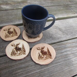 May include: Four wooden coasters with a moose design, each featuring a different pose of the moose. The coasters are arranged in a circle around a blue mug.