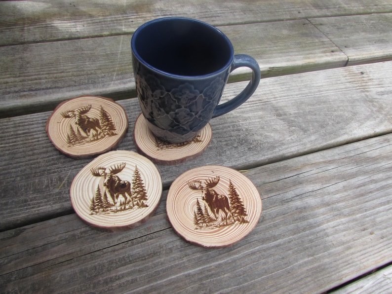 May include: Four wooden coasters with a moose design, each featuring a different pose of the moose. The coasters are arranged in a circle around a blue mug.