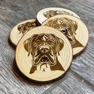 Puede incluir: Juego de cuatro posavasos de madera con un retrato de perro grabado. Los posavasos redondos están hechos de rodajas de madera natural y presentan una imagen detallada de la cara de un perro. Los rasgos del perro son de color marrón oscuro.