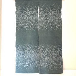 Könnte beinhalten: Zwei Stoffbahnen in einem gedämpften Türkis, vermutlich ein Vorhang oder Raumteiler. Das Design zeigt eine weiße, stilisierte Darstellung von hohem Gras und kleinen, gepunkteten Blumen. Die Paneele hängen an einer Holzstange.