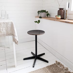 Op de afbeelding: Een ronde, zwarte houten tafel met een stervormige basis. De tafel staat in een witte kamer met witte muren en een witte vloer.