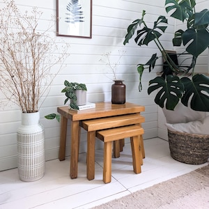 Può includere: Un set di tre tavolini in legno ad incastro con finitura naturale. I tavoli sono quadrati con gambe robuste, progettati per incastrarsi perfettamente. Il tavolo più grande misura circa 46 cm di larghezza, 46 cm di profondità e 46 cm di altezza. I tavoli sono esposti in una stanza luminosa e ariosa.