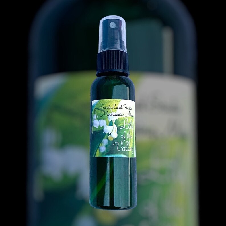 May include: A green glass bottle with a black spray top and a white label that reads "Sandy Land Studio Moisturizing Mist Lily of the Valley". The label features a watercolour illustration of lily of the valley flowers.