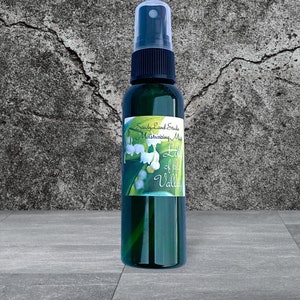 May include: A green glass bottle with a black spray top and a white label that says "SandyLand Studio Moisturizing Mist Lily of the Valley". The label has a picture of lily of the valley flowers.