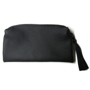 May include: A black, rectangular cosmetic bag with a zipper closure and a tassel. The bag has a textured surface and is set against a white background. The tassel is attached to the zipper pull.