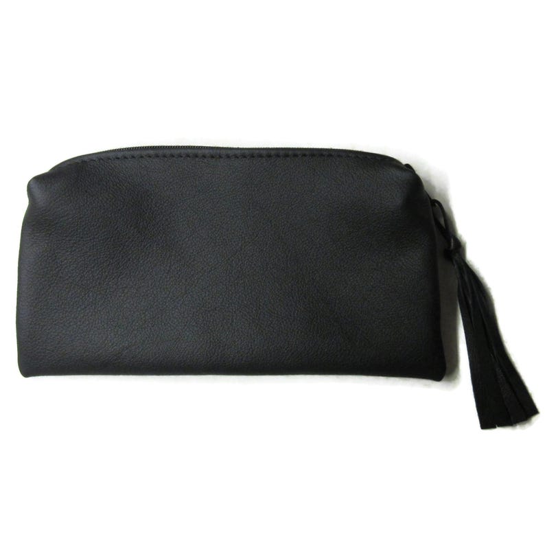May include: A black, rectangular cosmetic bag with a zipper closure and a tassel. The bag has a textured surface and is set against a white background. The tassel is attached to the zipper pull.
