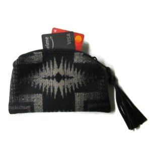 May include: A black and gray patterned zippered pouch with a black tassel. Two credit cards are partially visible inside the pouch. The pouch has a geometric design.