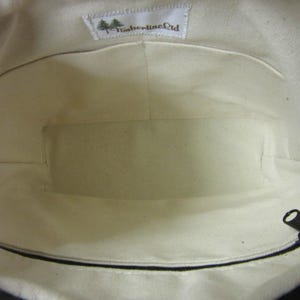 May include: Inside view of a canvas tote bag with a cream-coloured lining. The bag features a zipped pocket and a small label with the text "Timberline Ltd". The bag's interior has multiple compartments.