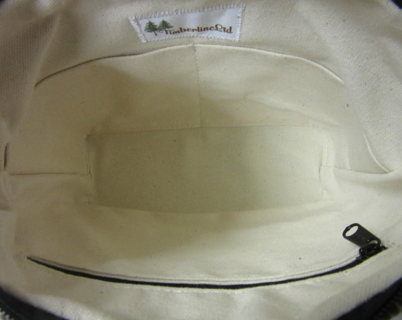 May include: Inside view of a canvas tote bag with a cream-coloured lining. The bag features a zipped pocket and a small label with the text "Timberline Ltd". The bag's interior has multiple compartments.