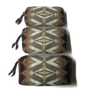 May include: Three different sized zippered pouches with a geometric pattern in shades of brown, beige, and red. The pouches have a fringe tassel with beads.