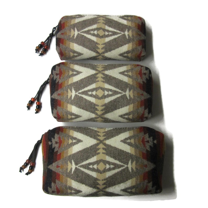 May include: Three different sized zippered pouches with a geometric pattern in shades of brown, beige, and red. The pouches have a fringe tassel with beads.