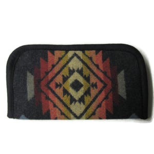 May include: A rectangular eyeglass case with rounded corners and a black fabric border. The surface features a geometric diamond pattern in shades of charcoal gray, burnt orange, mustard yellow, and muted blue, creating a symmetrical design.