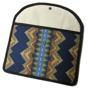 May include: A navy blue laptop sleeve with a geometric pattern in yellow, orange, and green. The sleeve has a cream-colored flap with a snap closure and a black trim. The design features a central vertical stripe.