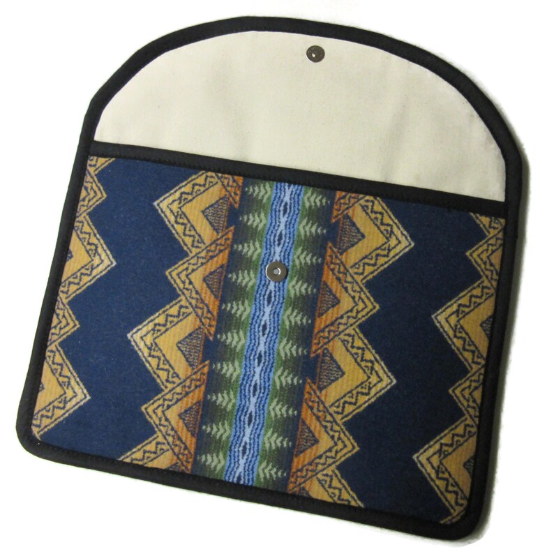 May include: A navy blue laptop sleeve with a geometric pattern in yellow, orange, and green. The sleeve has a cream-colored flap with a snap closure and a black trim. The design features a central vertical stripe.