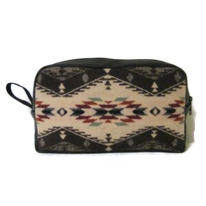 May include: A black and brown geometric patterned travel bag with a black leather zipper and handle.