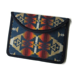 May include: A blue and orange patterned fabric clutch with a flap closure. The fabric has a geometric design with a southwestern style.