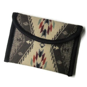May include: A rectangular, patterned clutch with a flap closure. The clutch features a cream-colored background with a geometric design in shades of brown, red, and blue. The edges are trimmed with black fabric.