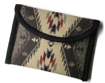 May include: A rectangular, patterned clutch with a flap closure. The clutch features a cream-colored background with a geometric design in shades of brown, red, and blue. The edges are trimmed with black fabric.