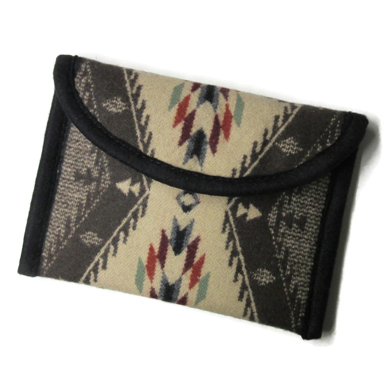 May include: A rectangular, patterned clutch with a flap closure. The clutch features a cream-colored background with a geometric design in shades of brown, red, and blue. The edges are trimmed with black fabric.