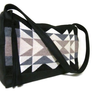 May include: Black shoulder bag with a geometric pattern in shades of gray, white, and brown. The bag has a long, black strap and a rectangular shape. The geometric design is on the front of the bag.