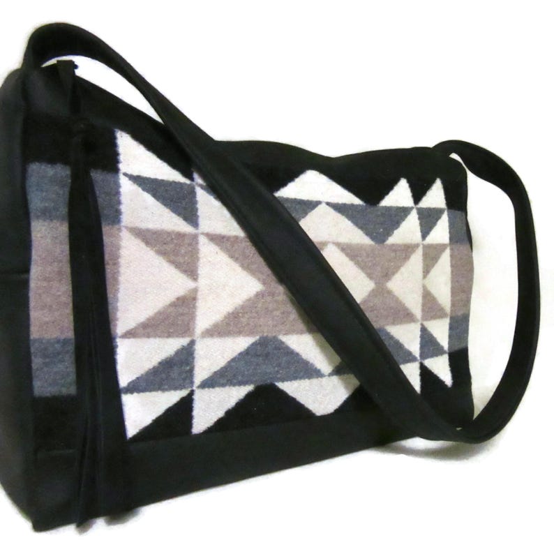 May include: Black shoulder bag with a geometric pattern in shades of gray, white, and brown. The bag has a long, black strap and a rectangular shape. The geometric design is on the front of the bag.