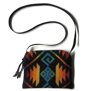 May include: A small, black crossbody bag with a colorful geometric pattern in shades of red, orange, yellow, green, and blue. The bag has a black strap and a zipper closure. The bag is approximately 7 inches wide and 5 inches tall.