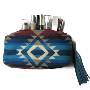 May include: A rectangular cosmetic bag with a geometric pattern in shades of blue, red, and beige. The bag is filled with various cosmetic products and has a blue tassel attached to the zipper.