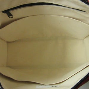 May include: Open view of a tote bag interior with multiple pockets. The bag's interior is a light beige color, with a black zipper and a dark patterned exterior. The pockets are sewn into the sides of the bag.