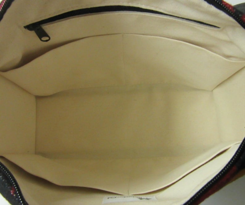May include: Open view of a tote bag interior with multiple pockets. The bag's interior is a light beige color, with a black zipper and a dark patterned exterior. The pockets are sewn into the sides of the bag.