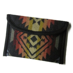 May include: A rectangular, gray clutch with a geometric pattern in shades of red, orange, yellow, and green. The clutch has a black border and a flap closure. The design features diamond and zigzag shapes.