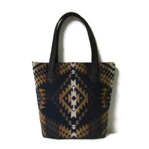 May include: A black tote bag with leather handles and a geometric pattern in shades of brown, beige, and white on a navy blue background.