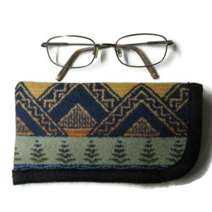 May include: Eyeglasses with a metal frame and brown temples rest above a patterned glasses case. The case features a geometric design in shades of blue, yellow, and green, with a black border. The glasses case is designed to protect the eyeglasses.