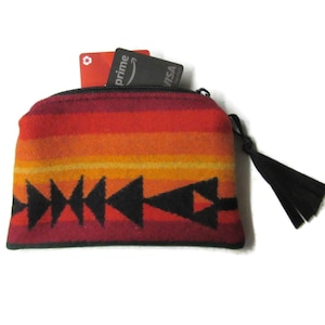 May include: A small, zippered pouch with a colorful, geometric design. The pouch features a gradient of red, orange, and yellow hues, with black triangle patterns. Two credit cards are visible inside the pouch. A black tassel hangs from the zipper.