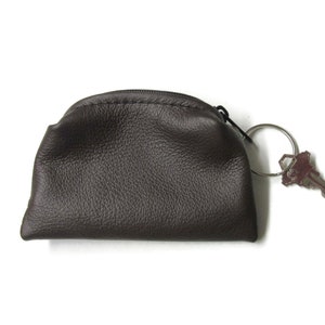 K&ouml;nnte beinhalten: Eine braune Lederm&uuml;nzb&ouml;rse mit Rei&szlig;verschluss und einem silbernen Schl&uuml;sselring.