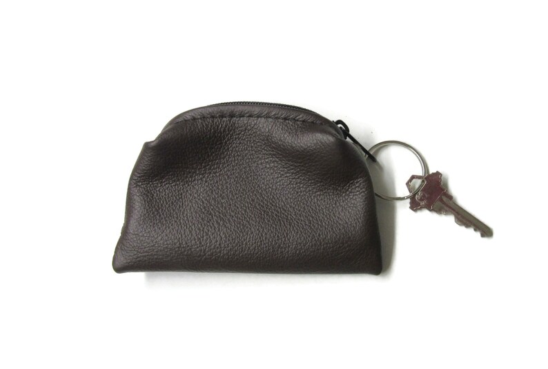 K&ouml;nnte beinhalten: Eine braune Lederm&uuml;nzb&ouml;rse mit Rei&szlig;verschluss und einem silbernen Schl&uuml;sselring.