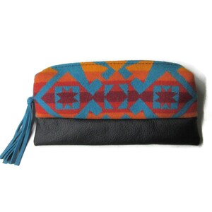 K&ouml;nnte beinhalten: Eine rechteckige Clutch mit schwarzem Lederboden und gemustertem Oberteil. Das Oberteil hat ein geometrisches Design in Orange, T&uuml;rkis und Burgunder. Eine t&uuml;rkisfarbene Quaste h&auml;ngt an der Seite.