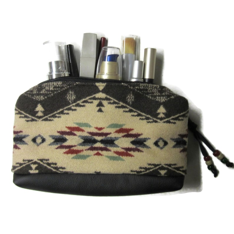 Op de afbeelding: Een kleine, bedrukte make-uptas met een zwarte leren bodem en een ritssluiting. De tas is gevuld met diverse make-up artikelen. Het patroon bestaat uit geometrische vormen in bruin, cr&egrave;me, rood en blauw. Een trekkoord met kralen is bevestigd.