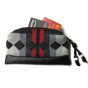 May include: A small black zippered pouch with a red, black, and white patterned fabric exterior. The pouch has a black leather bottom and a black drawstring with brown and white beads. Two credit cards are visible in the pouch.