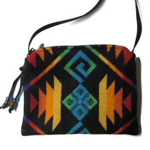 Pu&ograve; includere: Una borsa a tracolla nera con un vivace motivo geometrico in rosso, arancione, giallo, verde e blu. La borsa ha una tracolla nera e una chiusura a cerniera. Un piccolo nappa di perline pende dal lato.
