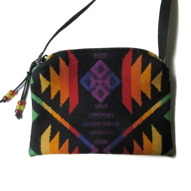 Puede incluir: Bolso bandolera negro con un colorido estampado geom&eacute;trico en tonos rojos, naranjas, amarillos, verdes y morados. Tiene una correa negra, cierre de cremallera y adornos de cuentas. El bolso mide aproximadamente 20 cm de ancho y 15 cm de alto.