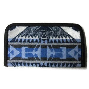 May include: Rectangular, patterned textile in shades of blue, gray, and white. The design features geometric shapes, including triangles and diamond-like figures. A black border frames the edges of the textile.