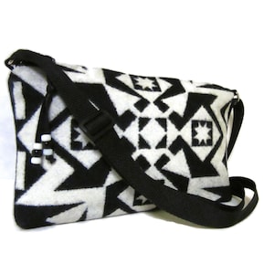 May include: A black and white geometric patterned crossbody bag with a black adjustable strap. The bag has a white tassel with black and white beads.